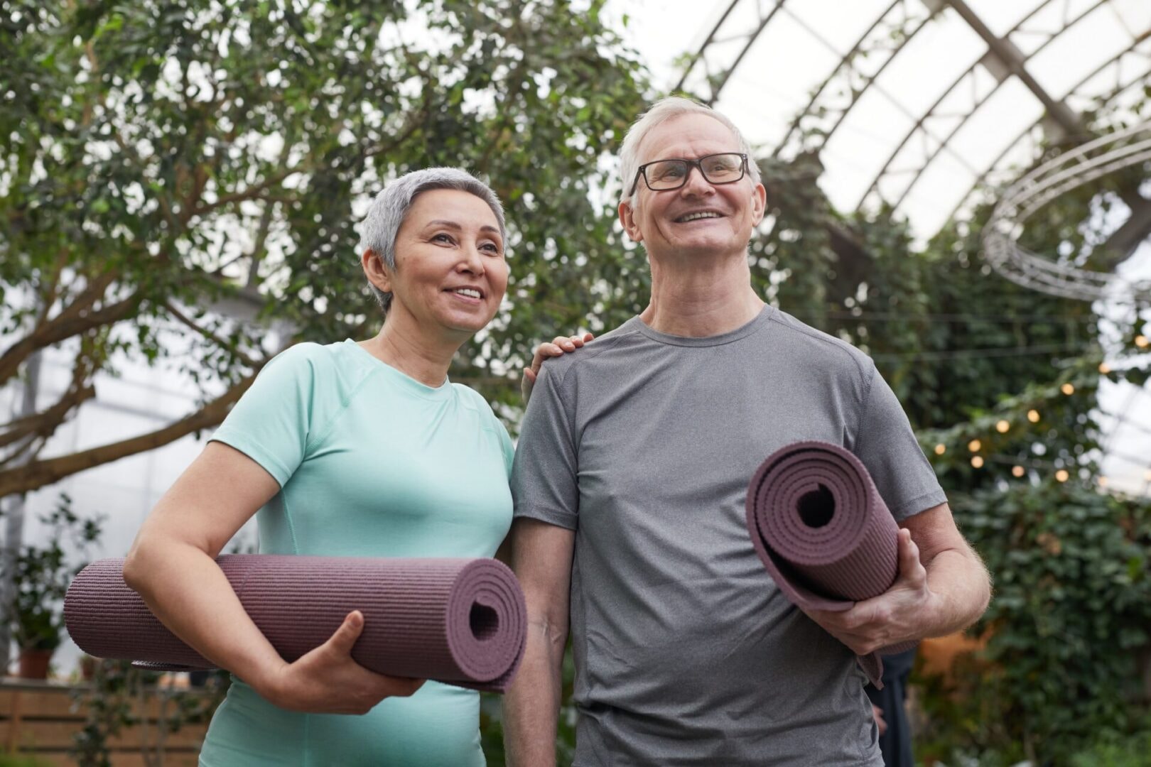 Senior couple with yoga mats in a greenhouse